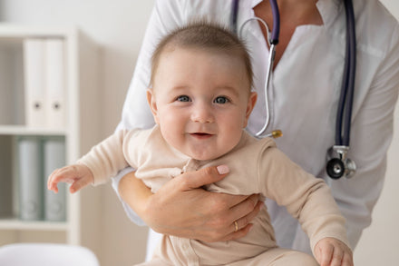 Baby being held by a person wearing a white lab coat and a stethoscope around their neck 